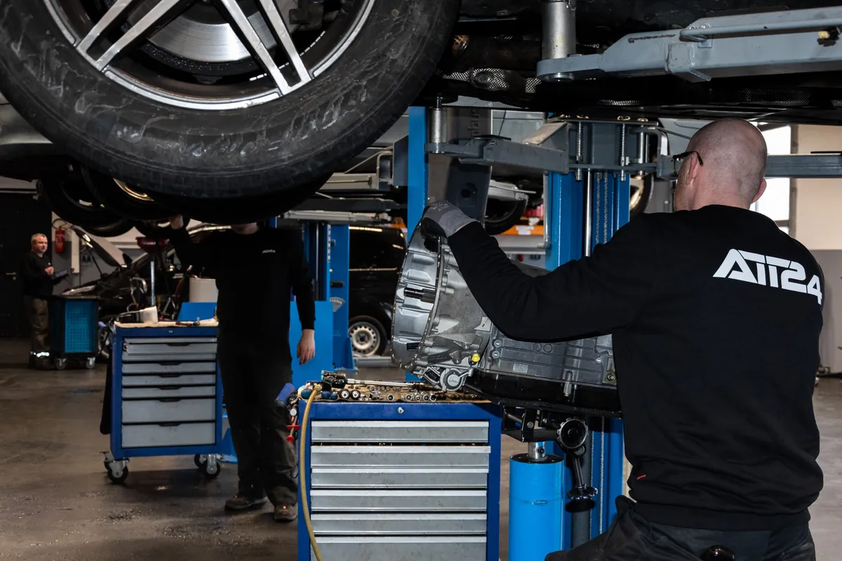 Mitarbeiter im ATT24-Pullover setzt ein Getriebe unter einem Mercedes an